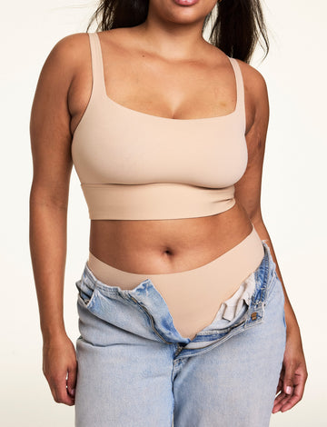 In a studio setting, Gianna wears the Bliss Square Neck Bralette in Beige with matching underwear and unbuttoned light wash jeans, showcasing the square neckline, smooth fabric, and wide supportive band. sizing: Alana wears size Large