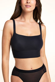 In a studio setting, Laura wears the Bliss Square Neck Bralette in Black, featuring a square neckline, wide straps, and a longline underband in smooth microfiber fabric for wireless support and all-day comfort, paired with sheer mesh underwear.