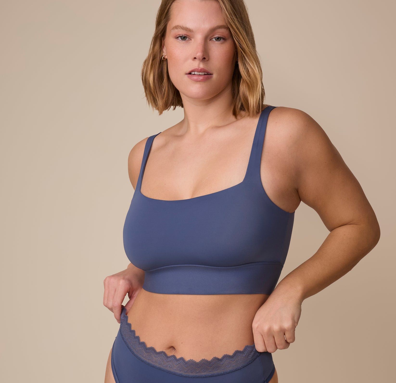 Sonnie wearing the Bliss Square Neck Bralette and Bliss Lace Highwaist Thong in Twilight. She gently adjusts the waistband of the underwear, showcasing the bralette's flattering and supportive silhouette. sizing: Sonnie wears size XL