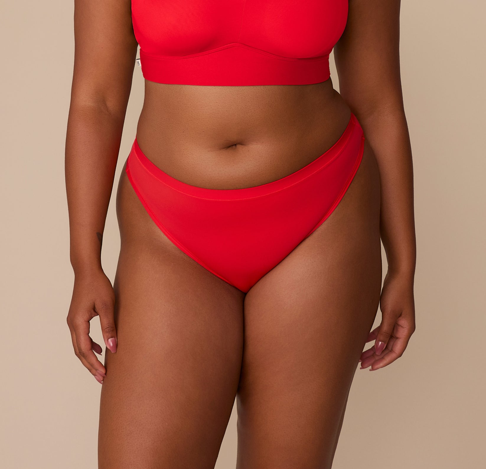 Front view of Zarria wearing the Bliss Thong in Cherry. The image highlights the high-cut leg and smooth microfiber waistband designed to sit comfortably on the hips. sizing: Zarria wears size XL
