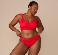 Zarria in a relaxed pose wearing the Bliss Triangle Bralette and Bliss Thong in Cherry. The image shows the coordinating set, highlighting the lightweight, second-skin fit of the thong.