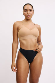 On a white studio backdrop, Amber wears the Bliss Thong in Black, paired with a nude Bliss bralette. The thong sits smoothly at the waist with a clean, minimal finish and a lightweight, second-skin look.  sizing: Amber wears size Large