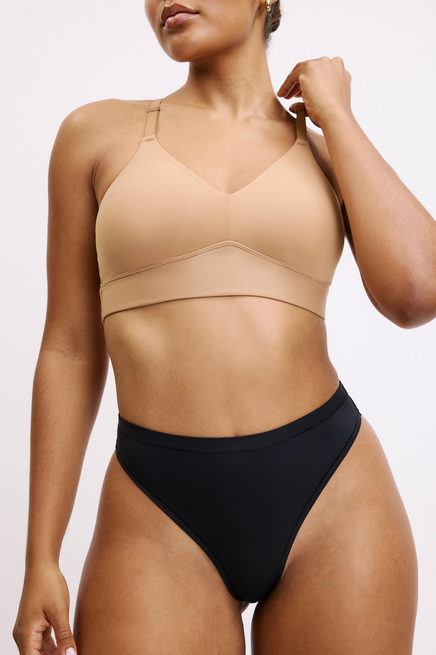 On a white studio backdrop, Amber wears the Bliss Thong in Black, shown from the front. The wireless bralette features a smooth V-neck and adjustable straps, paired with the thong’s clean waistband and minimal front coverage in soft microfiber fabric.