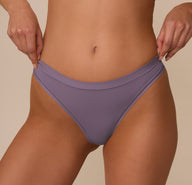 Close-up of the Bliss Thong in Eclipse worn by Marcela, focusing on the waistband detail and seamless side construction for a no-show fit beneath clothing.