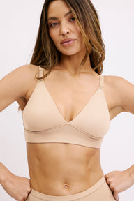 On a white studio backdrop, Darion wears the Bliss Triangle Bralette in Beige, showing the deep V neckline, lightly supportive wireless band, and smooth microfiber fabric. sizing: Darion wears size Small