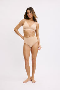 On a white studio backdrop, Darion wears the Bliss Triangle Bralette in Beige with matching bottoms, highlighting the pullover design, low-coverage triangle shape, and clean, minimal silhouette.