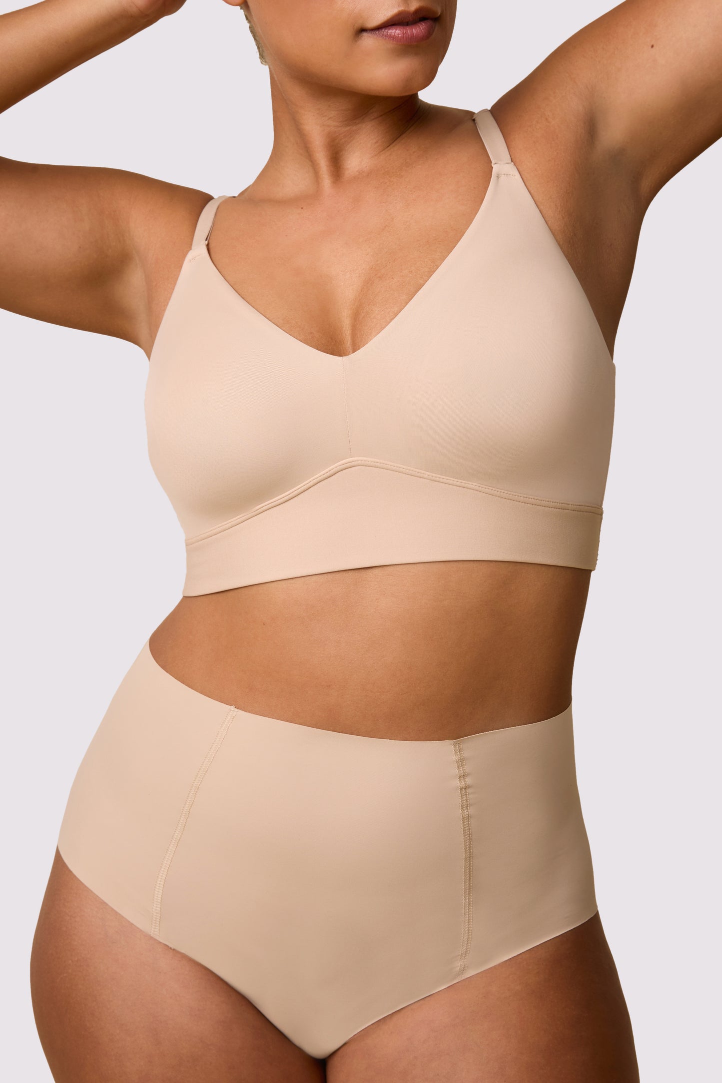 On a white studio backdrop, India wearsthe Bliss Triangle Bralette in Beige with the matching brief, showing the deep V neckline, smooth microfiber fabric, and wireless band.