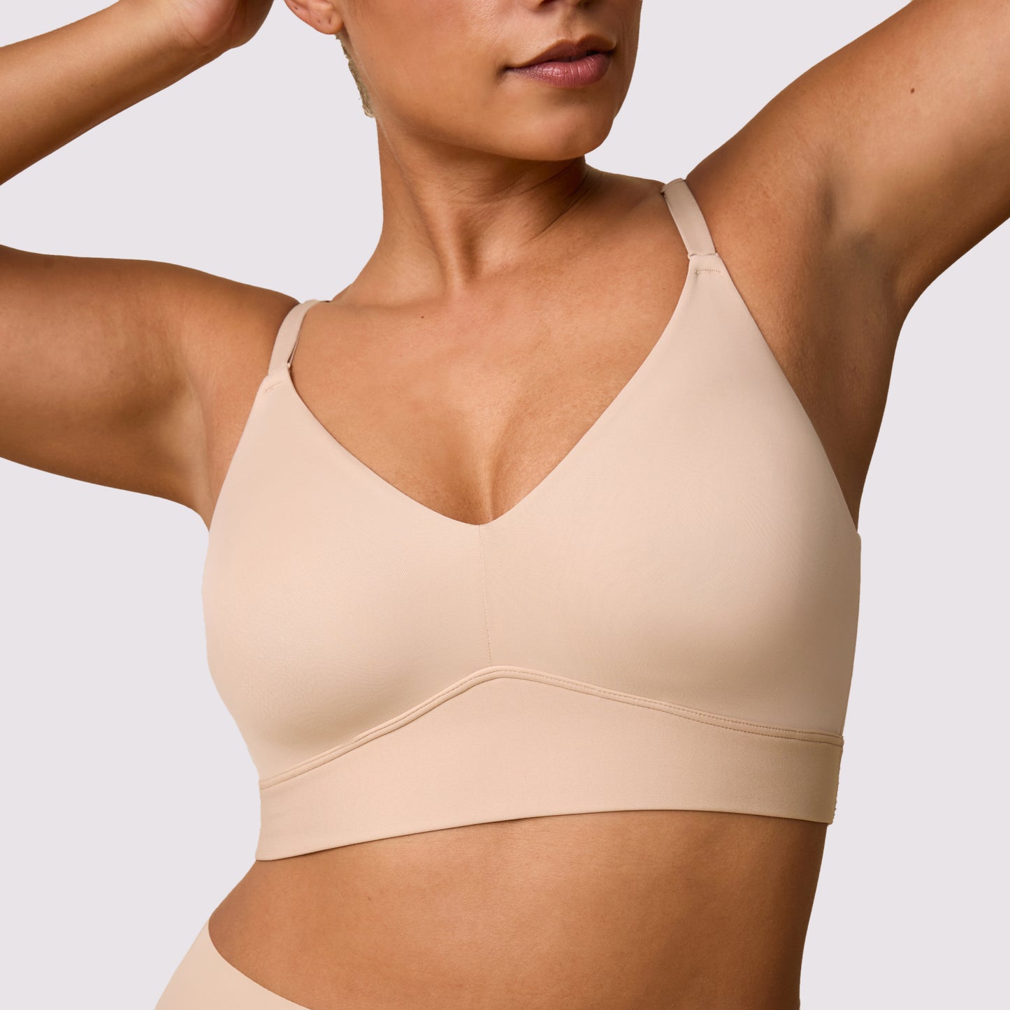 On a white studio backdrop, India wears the Bliss Triangle Bralette in Beige, highlighting the pullover design, front-adjusting straps, and lightly supportive wireless lift.