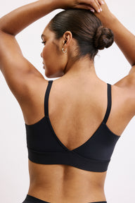 From the back on a white studio backdrop, Amber wears the Bliss Triangle Bralette in Black, showing the low-back V shape, adjustable straps, and smooth microfiber band.