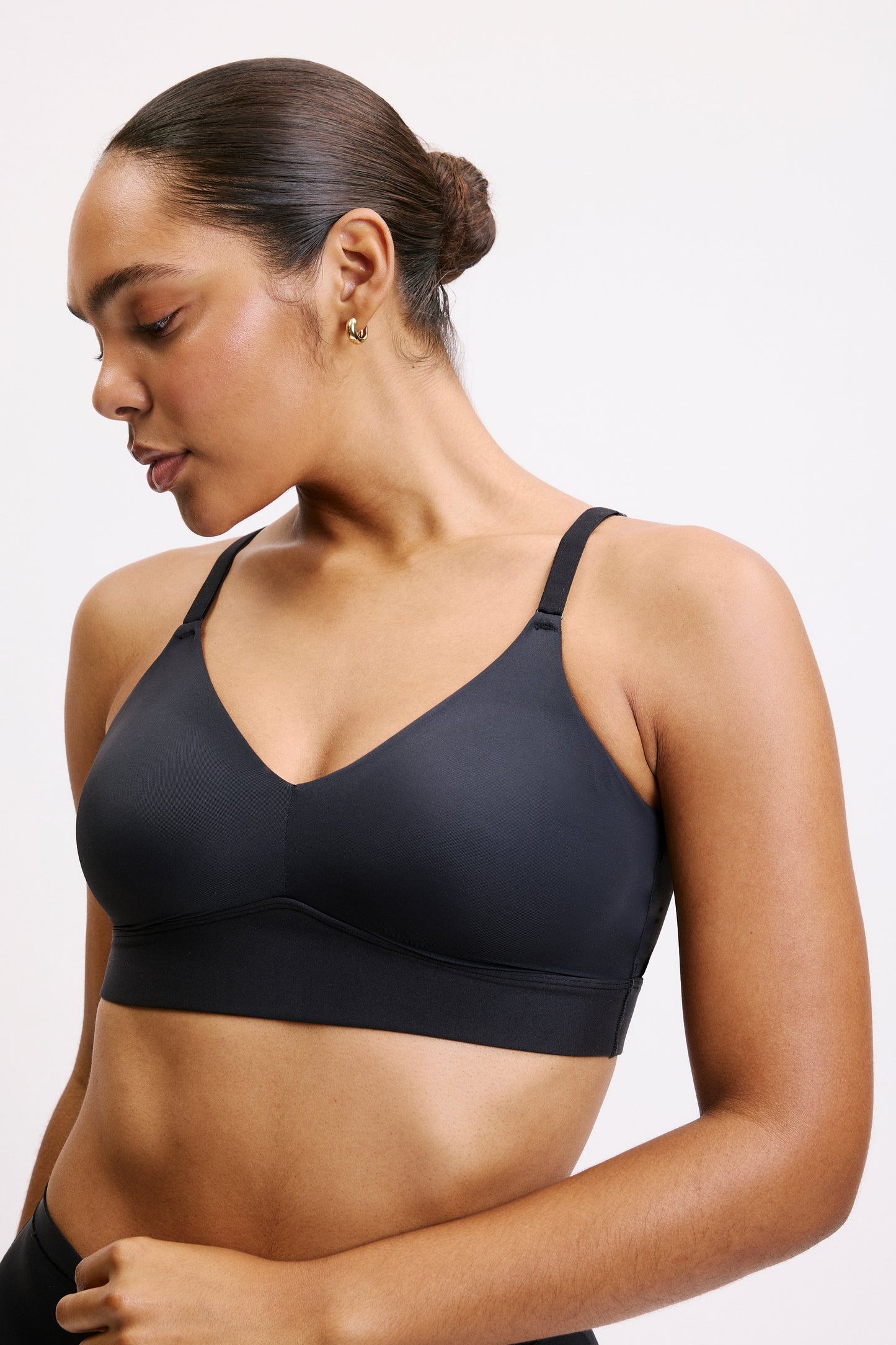 In a three-quarter studio view on a white backdrop, Amber wears the Bliss Triangle Bralette in Black, showing the deep V neckline, smooth microfiber fabric, and wireless band.