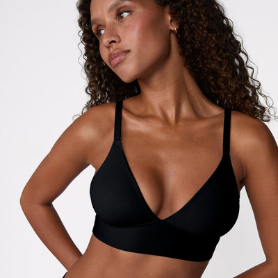 In a white studio setting, Courtney wears the Bliss Triangle Bralette in Black, shown in a close-up to highlight the clean V-neck shape, wireless band, and soft microfiber fabric.