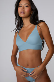 On a light gray studio backdrop, Amber wears the Bliss Triangle Bralette in Poolside with the matching bikini brief. The pullover bralette shows a deep V neckline, adjustable front straps, and a smooth microfiber band. sizing: Amber wears size XS