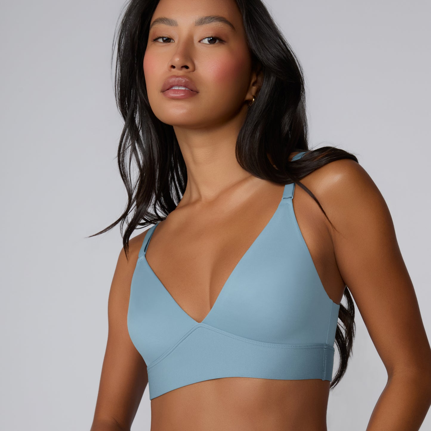 On a light gray studio backdrop, Amber models the Bliss Triangle Bralette in Poolside, shown from the waist up to highlight the deep V front, soft microfiber fabric, and wide wireless band.