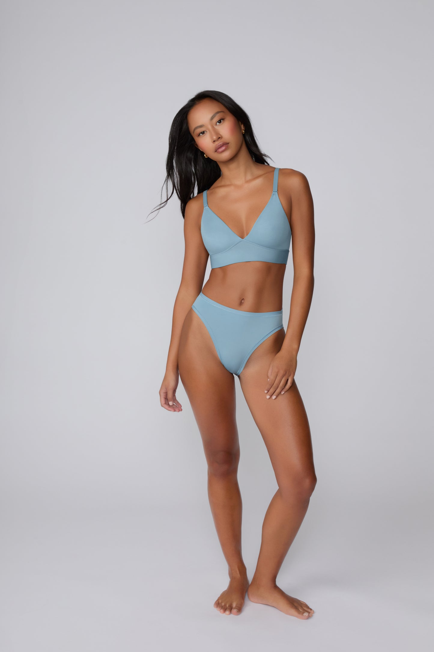 Full-body view on a light gray studio backdrop of Amber wearing the Bliss Triangle Bralette in Poolside with the coordinating bikini brief, showing the lightweight pullover design and adjustable straps.