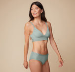 Anna turns slightly to the side, wearing the Bliss Triangle Bralette in Seaglass. The supportive fit offers a functional design. sizing: Anna wears size Small. Sizes L-6XL have higher center in front for additional support.