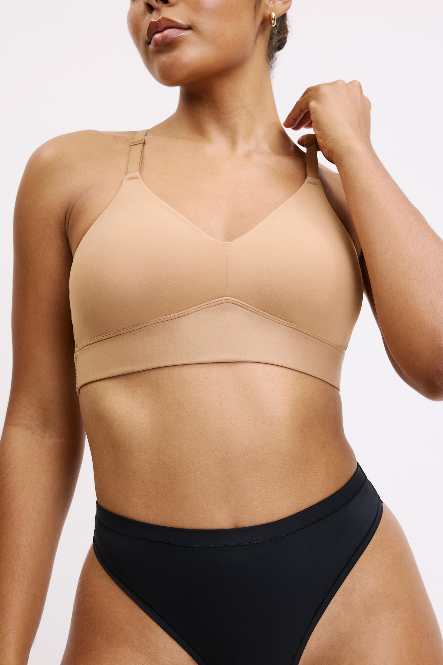 On a white studio backdrop, a close front view shows Amber wearing the Bliss Triangle Bralette in Tan. The triangle shape and clean neckline are visible, designed to sit smoothly under clothing.