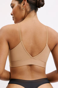 On a white studio backdrop, a back close-up shows Amber wearing the Bliss Triangle Bralette in Tan. The adjustable straps and smooth back band are visible, designed to sit comfortably against the skin.
