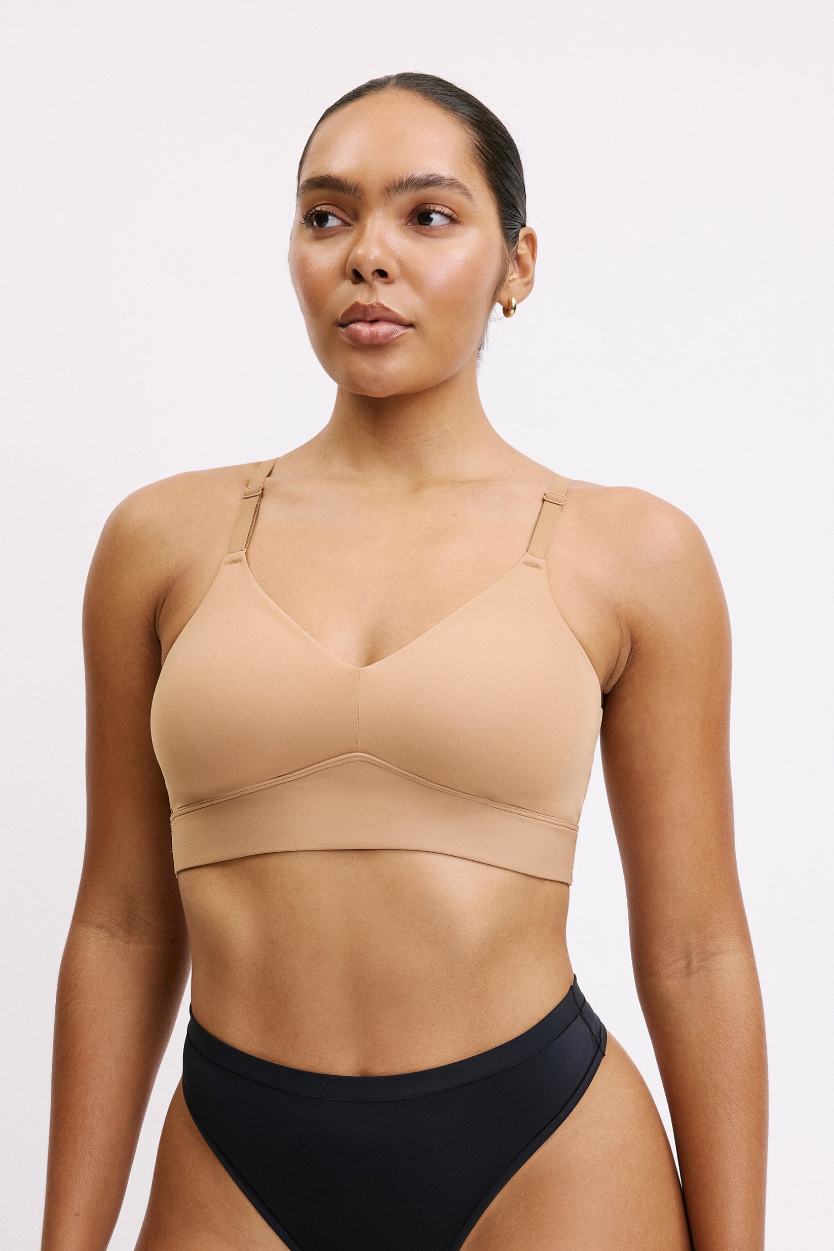 On a white studio backdrop, Amber wears the Bliss Triangle Bralette in Tan, showing the deep V-neckline, smooth microfiber fabric, and front-adjusting straps designed for everyday comfort. sizing: Amber wears size Large