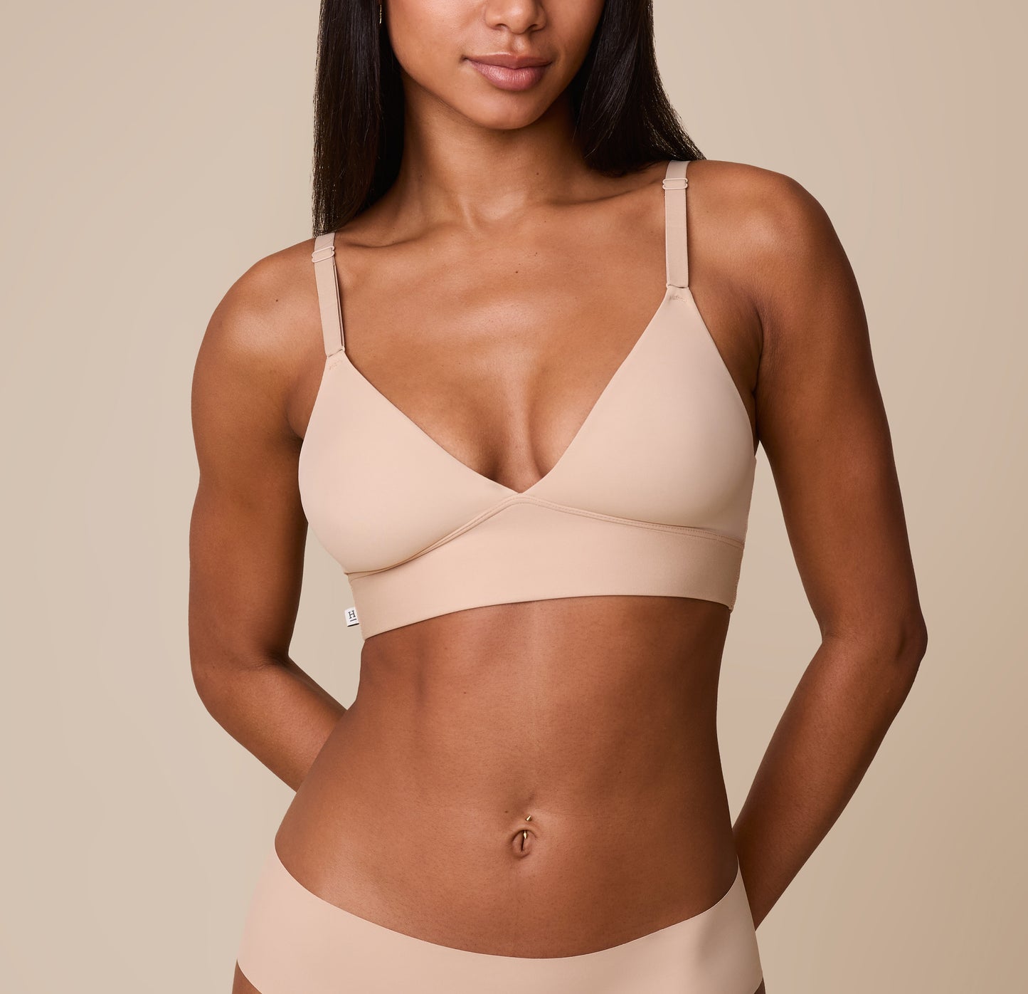 Ally wears the Bliss Triangle Bralette in Beige, showcasing the soft, wire-free cups, deep V-neckline, and supportive elastic underband against a neutral background. sizing: Ally wears size XS