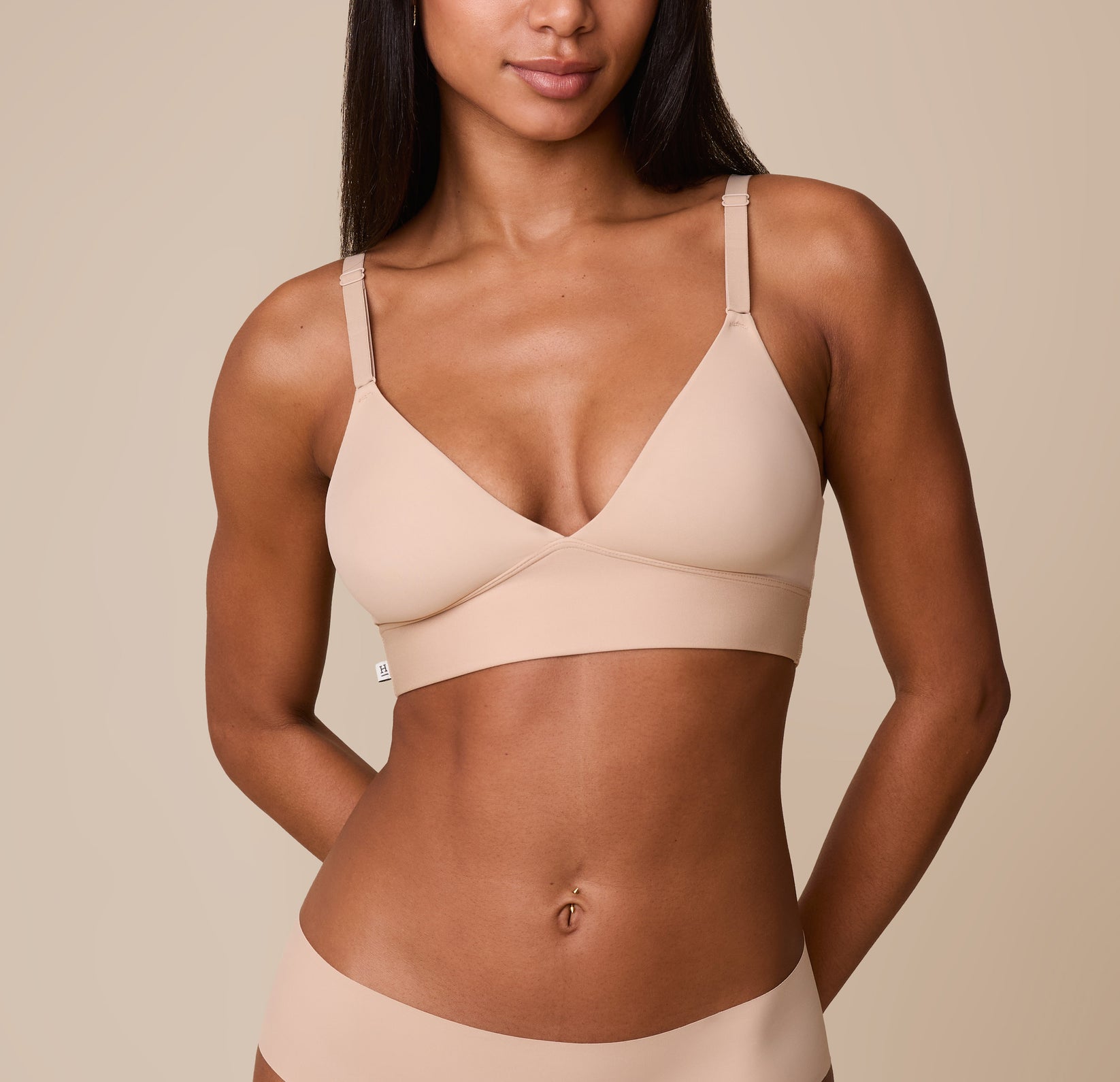 Ally wears the Bliss Triangle Bralette in Beige, showcasing the soft, wire-free cups, deep V-neckline, and supportive elastic underband against a neutral background. sizing: Ally wears size XS