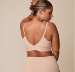 India faces away from the camera, showing the back of the Bliss Triangle Bralette in Beige with its soft, elastic band and low V neck back.