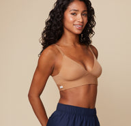 Ally poses at a three quarter angle wearing the Bliss Triangle Bralette in Tan. The sleek, seamless fabric and flattering triangular cup shape are emphasized.