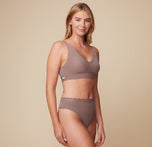  smiling while wearing the Bliss Lace Bralette and Bliss Highwaist Lace Thong in Mauve. The image captures a side view, emphasizing the comfortable fit of both pieces.