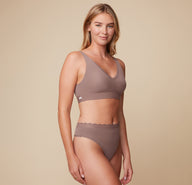  smiling while wearing the Bliss Lace Bralette and Bliss Highwaist Lace Thong in Mauve. The image captures a side view, emphasizing the comfortable fit of both pieces.