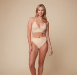 Model Megan wearing the Bliss Lace Halterneck Bralette in Beige, paired with the matching Bliss Highwaist Lace Thong. She stands facing forward, highlighting the soft, supportive fit of the halterneck bralette and thong. sizing: Sizes L-4XL have higher center in front for additional support.