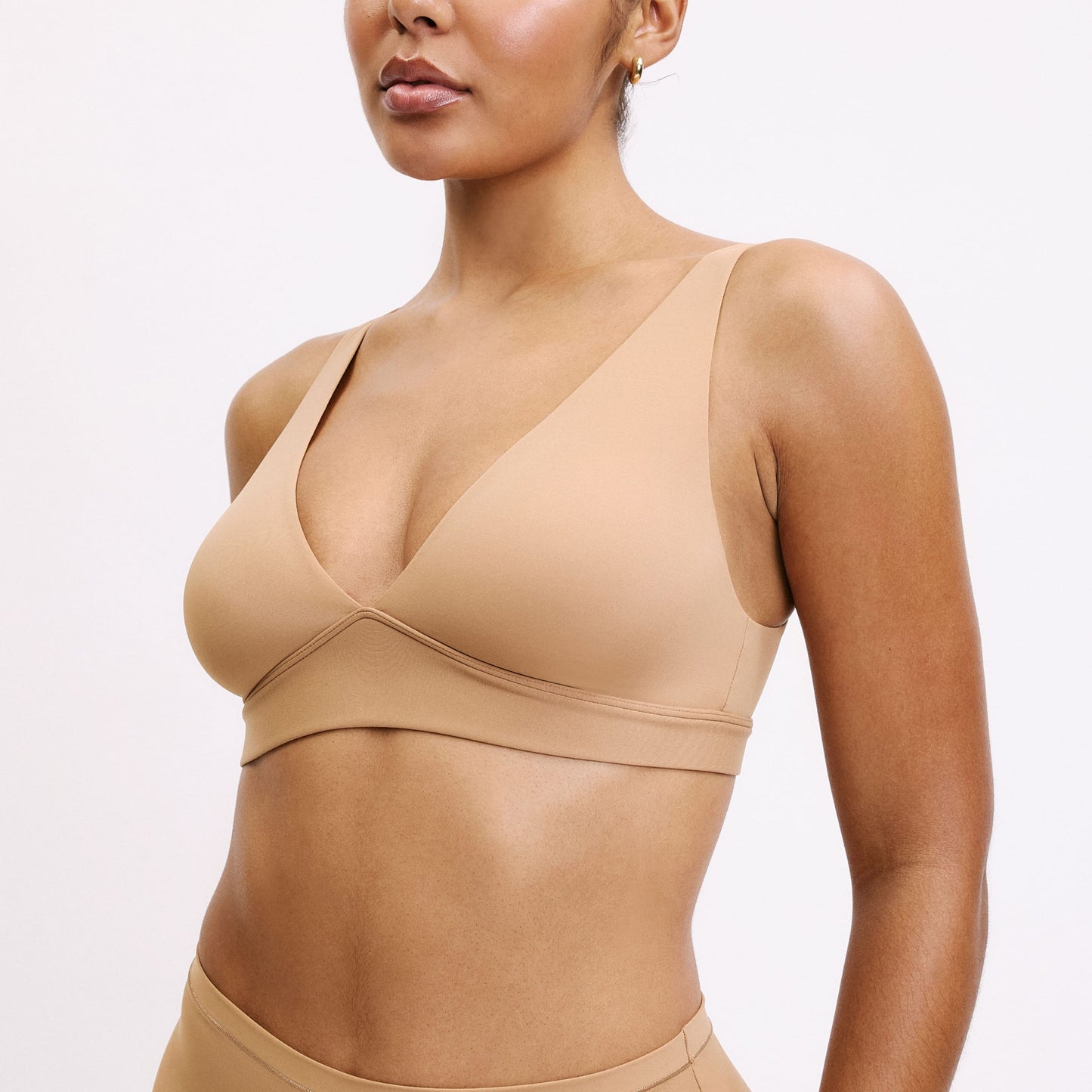 Amber wears the Bliss Plunge Adjustable Bra in Tan, highlighting the deep V neckline, smooth cups, and soft, wireless support.
