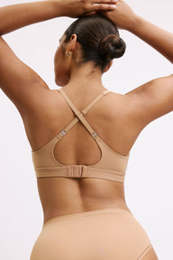 Amber wears the Bliss Plunge Adjustable Bra in Tan from the back with the J-hook fastened into a racerback, showing adjustable straps and a smooth microfiber band.