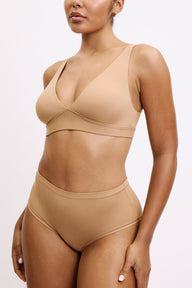 Amber wears the Bliss Plunge Adjustable Bra in Tan with matching briefs, highlighting the deep V neckline, wireless support, and smooth, lightweight microfiber fabric.