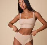 Ally wears the Bliss Square Neck Bralette in Beige, gently adjusting the waistband of her matching Bliss Highwaist Briefs. The smooth microfiber fabric lays flat, creating a sleek look. sizing: Ally wears size Small