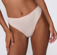 On a white studio backdrop, a close-up front view of the Bliss Thong in Ember Rose shows the smooth microfiber fabric, mid-rise waistband, and minimal-coverage thong silhouette. sizing: Courtney wears size Small
