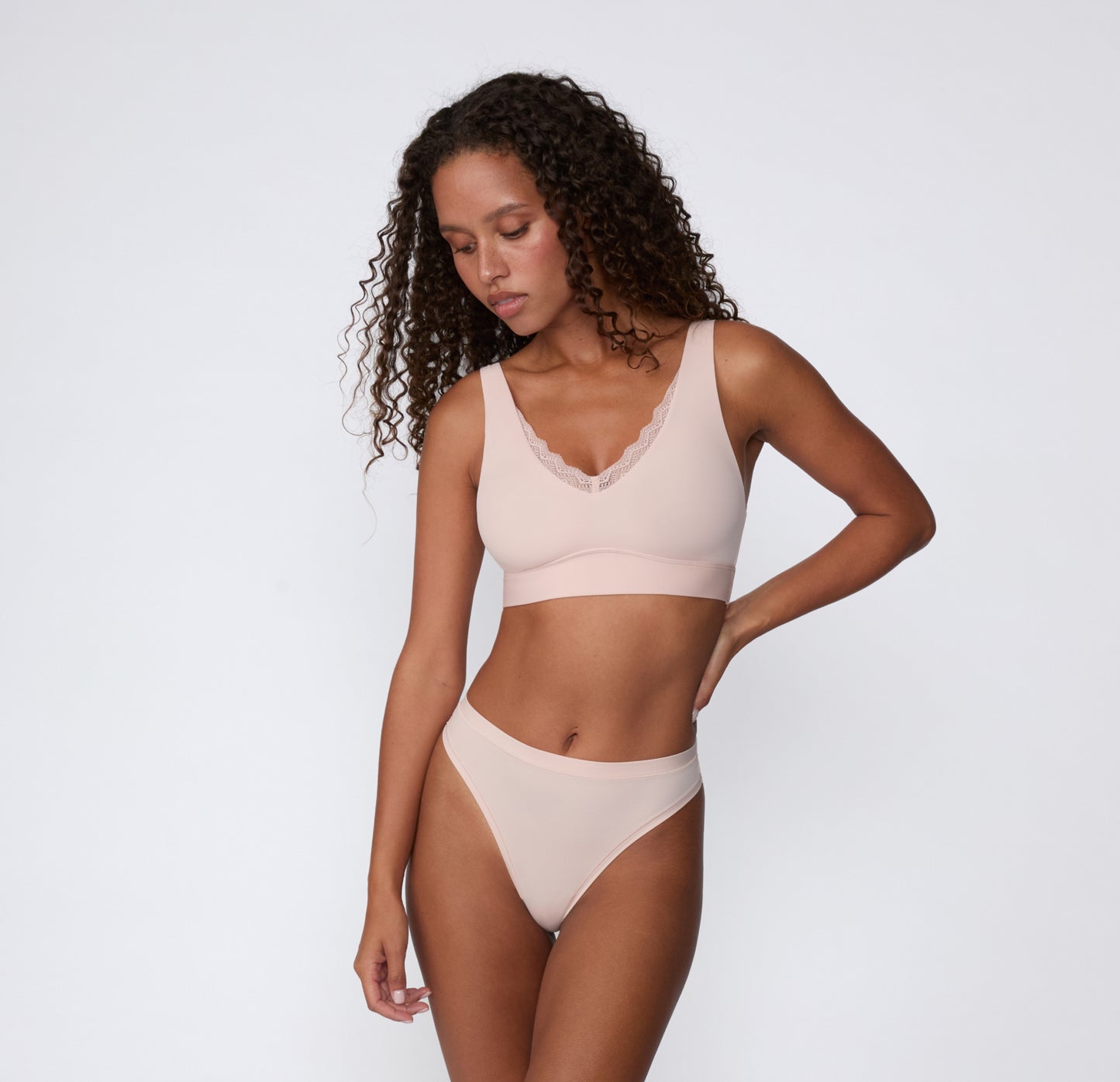 Full-body view on a white studio backdrop of a model wearing the Bliss Lace Bralette and Bliss Thong in Ember Rose, showing the coordinated set and smooth, wireless design.