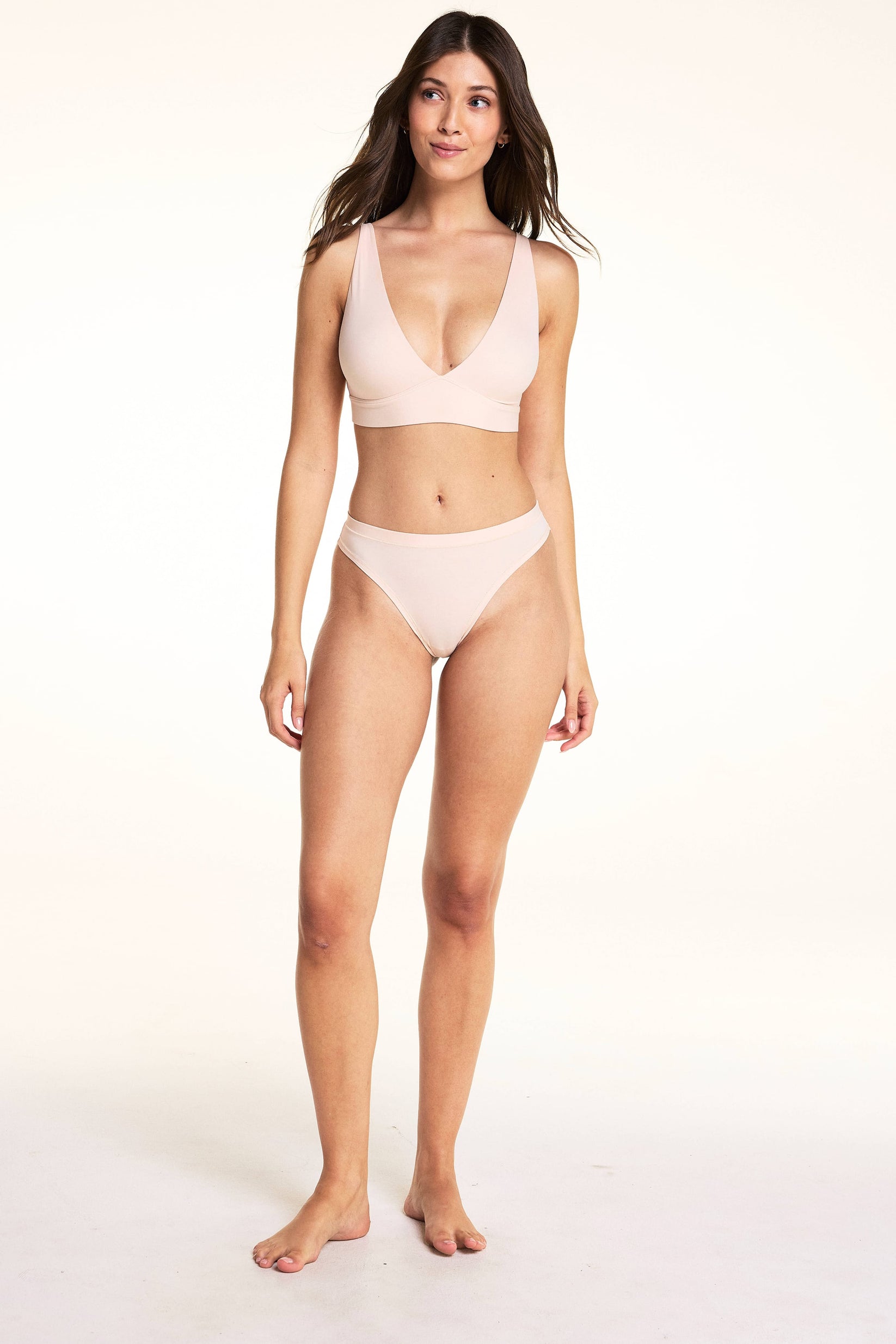 In a studio setting, Laura wears the Bliss Triangle Bralette and Bliss Thong in Rose, featuring a deep V-neckline, soft microfiber fabric, and a low-rise thong silhouette with minimal back coverage.