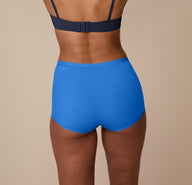 Nemesis wears the Bliss Boyshort in Bluebird, showing the full-coverage back and soft microfiber construction against a neutral studio backdrop.
