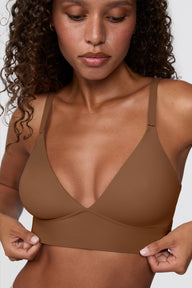 Close-up against a light grey backdrop, Courtney wears the Bliss Triangle Bralette in Brown, highlighting the deep V neckline, smooth microfiber fabric, and wide wireless band. sizing: Courtney wears size Small