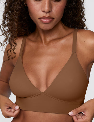 Close-up against a light grey backdrop, Courtney wears the Bliss Triangle Bralette in Brown, highlighting the deep V neckline, smooth microfiber fabric, and wide wireless band. sizing: Courtney wears size Small