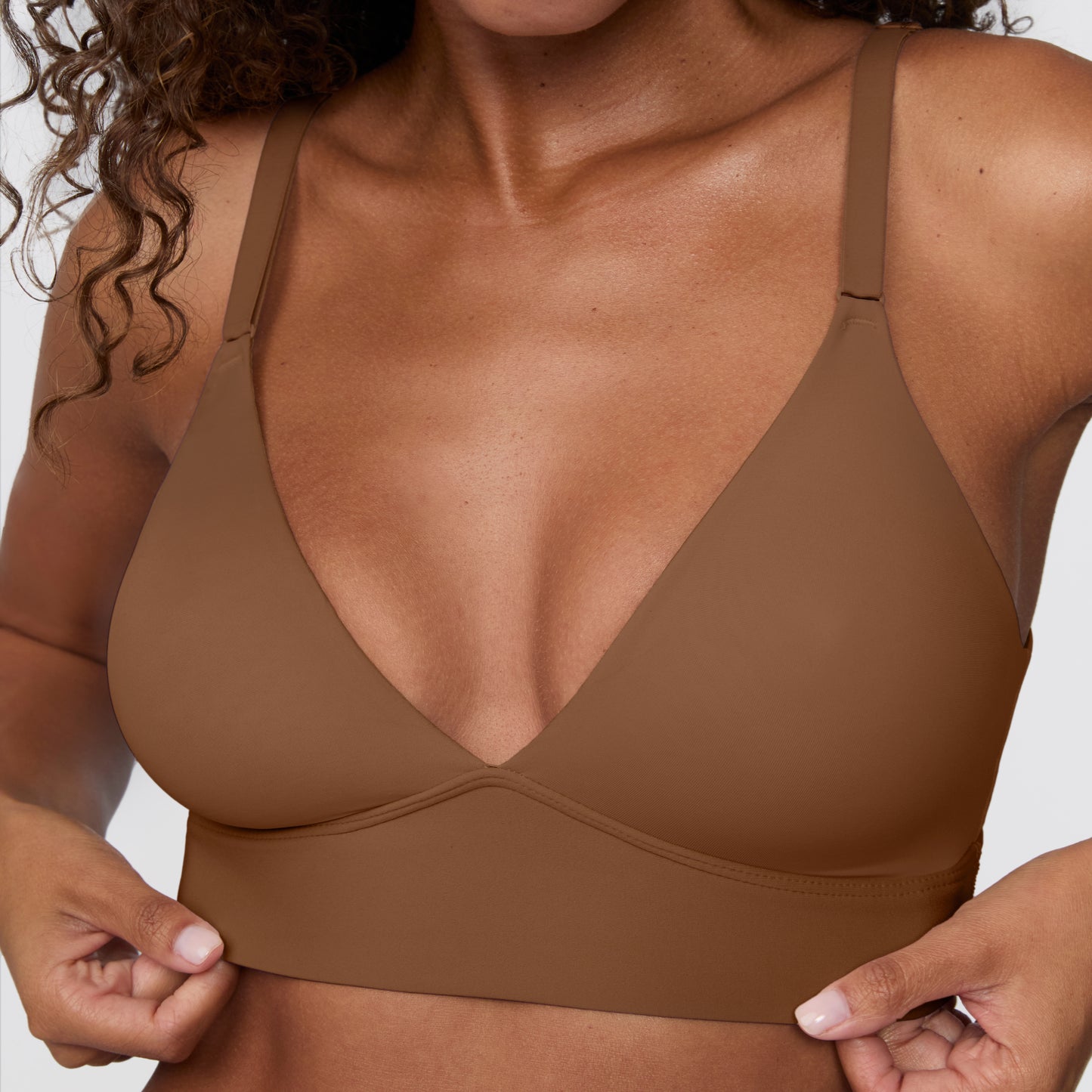 Close-up against a light grey backdrop, Courtney wears the Bliss Triangle Bralette in Brown, highlighting the deep V neckline, smooth microfiber fabric, and wide wireless band.