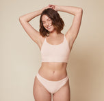 Carli standing with her arms raised, wearing the Bliss Racerback Bralette and Bliss Bikini in Rose. The front view highlights the comfortable and relaxed fit of the bralette and bikini. sizing: Carli wears size Medium