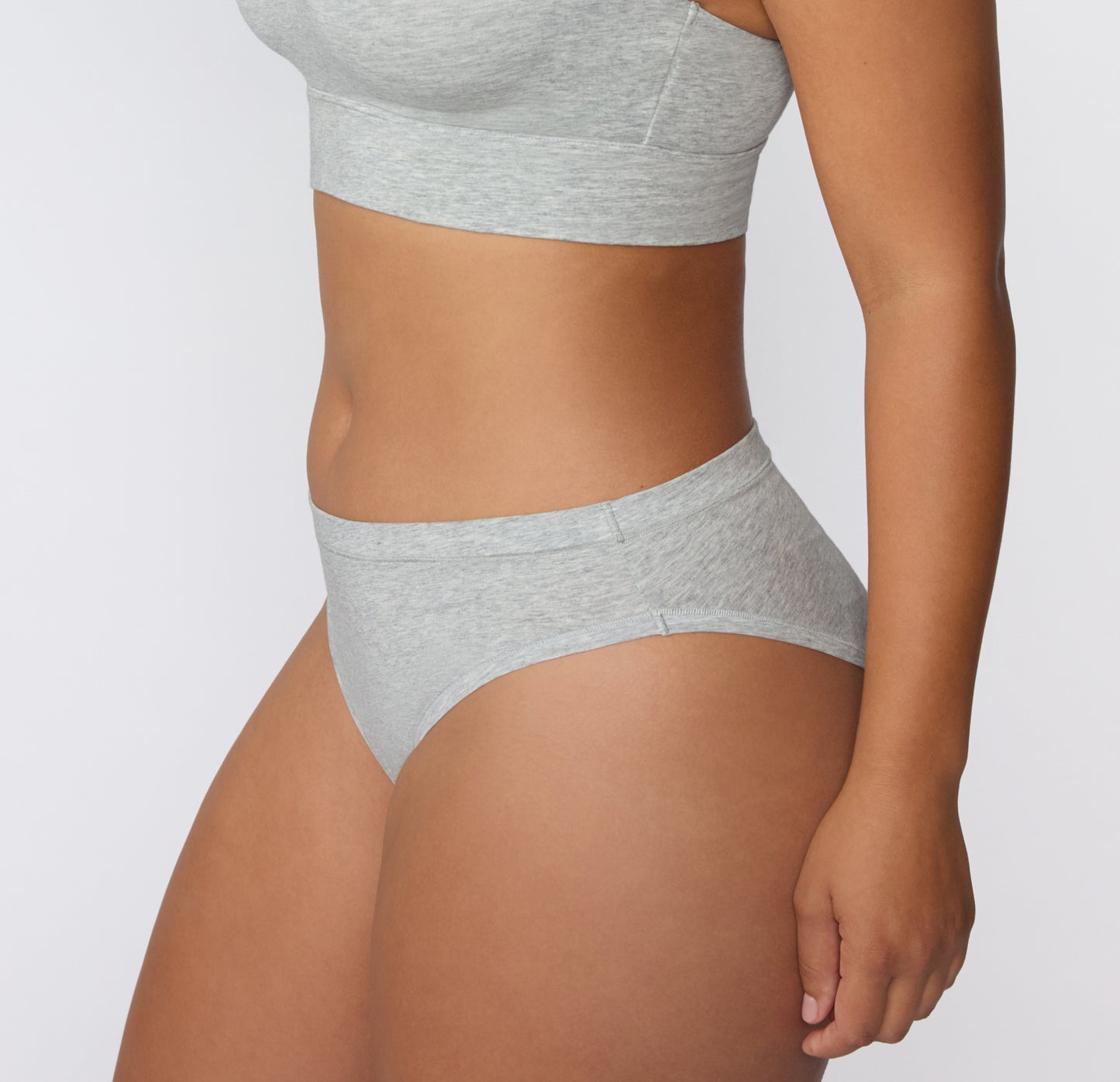 Side view on a light studio backdrop of the Cloud Cotton Bikini in Light Heather Grey, showing the low-rise fit and clean leg opening.