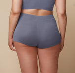 Back view of Bianca modeling the Cloud Cotton Triangle Bralette and Boyshort in Slate. She stands with her arms relaxed by her sides, highlighting the back details of the set.