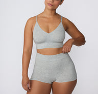 On a white studio backdrop, a model wears the Cloud Cotton Boyshort in Heather Grey paired with a matching cotton bralette, showing the high-rise waistband and everyday boyshort length.