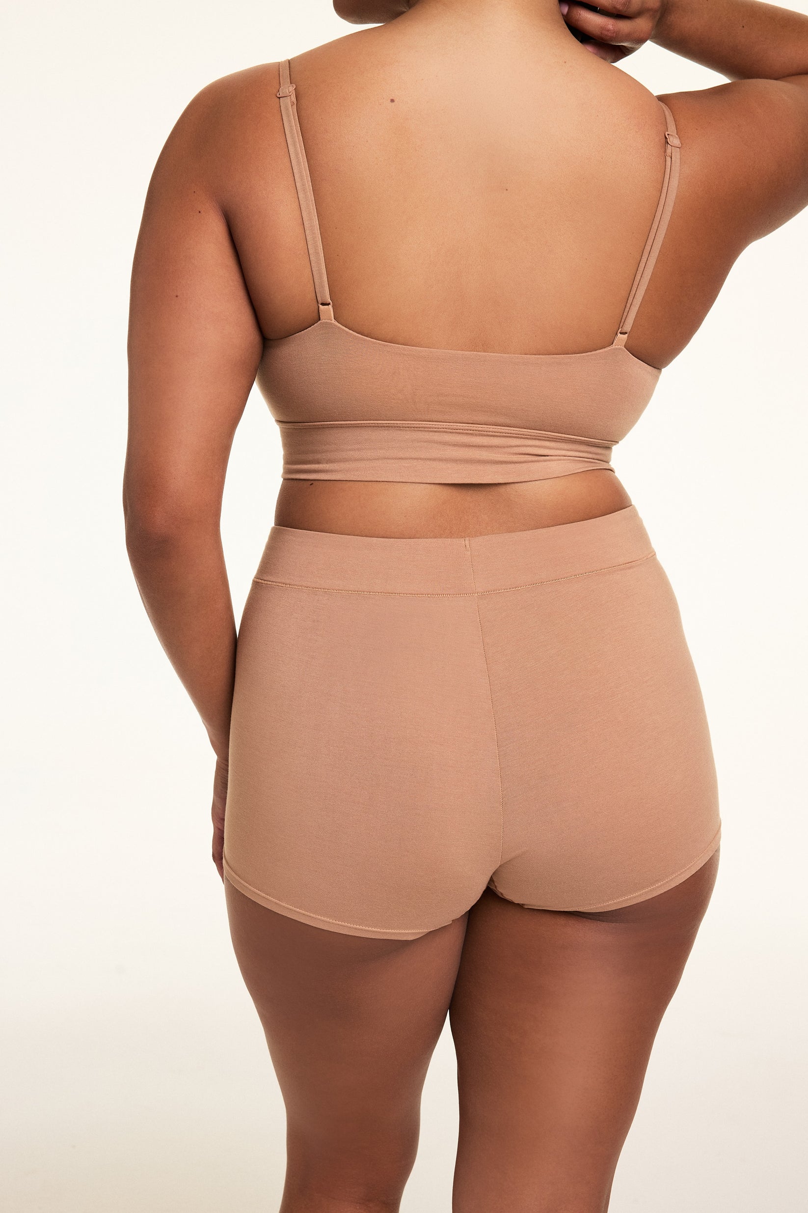 In a softly lit studio, Alana wears the Cloud Cotton Thin Strap Bralette and Cloud Cotton Highwaist Boyshort in Dune, shown from the back. The bralette features thin adjustable straps and a longline silhouette, while the high-waisted boyshort provides full coverage in soft, stretchy cotton modal fabric.