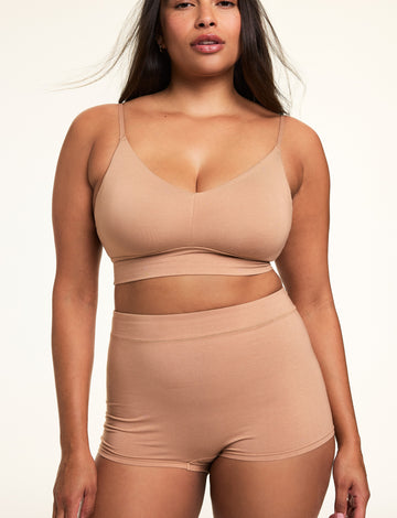 In a softly lit studio, Alana wears the Cloud Cotton Thin Strap Bralette and Cloud Cotton Highwaist Boyshort in Dune. The bralette features a square neckline, thin adjustable straps, and soft cotton modal fabric, paired with a high-waisted boyshort designed for full coverage and everyday comfort. sizing: Alana wears a size Large