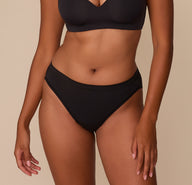 Victoria wears the Cloud Cotton French Cut Brief in Black, showcasing its mid-rise waistband and high-cut leg opening that elongates the legs and offers modern, breathable coverage. sizing: Victoria wears size Medium