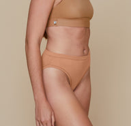 Three quarter angle of Erin with her arms down by her sides.  She’s wearing the Bliss Scoop Bralette in the color Tan and the Cloud Cotton French Cut Brief in the color Dune.