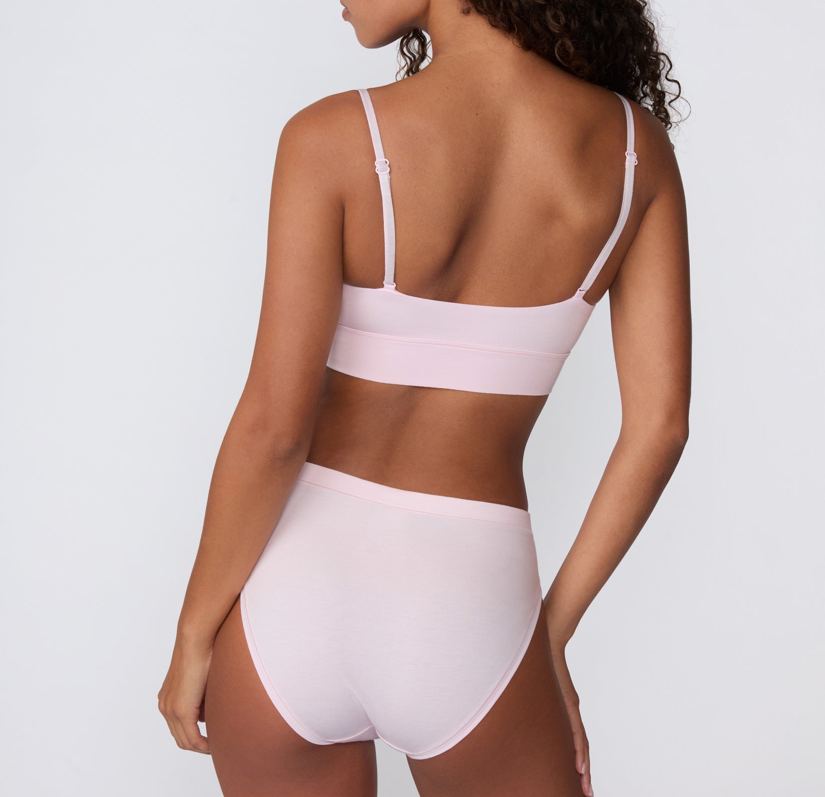 On a clean studio backdrop, a back view shows a model wearing the Cloud Cotton French Cut Brief in Primrose with the matching Cloud Cotton Thin Strap Bralette, featuring the smooth waistband and full back coverage.