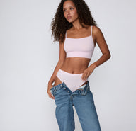 On a clean studio backdrop, a full-body view shows a model wearing the Cloud Cotton French Cut Brief in Primrose with the matching Cloud Cotton Thin Strap Bralette, styled with low-rise denim.
